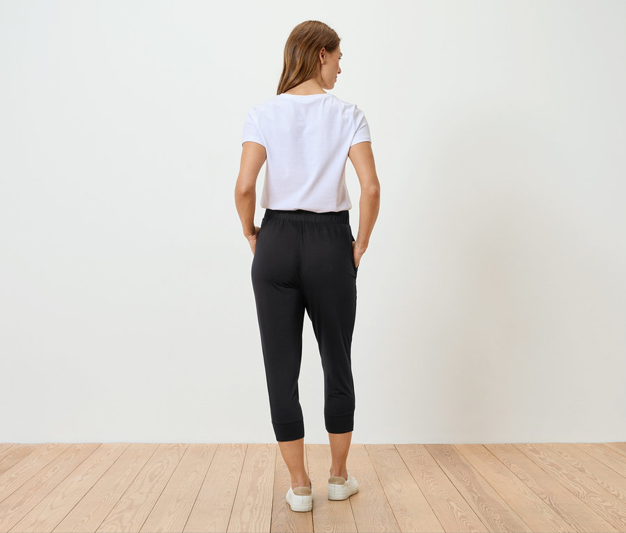 Frau von hinten in einem weißen T-Shirt und einer schwarzen Hose, die auf einem Holzboden steht.