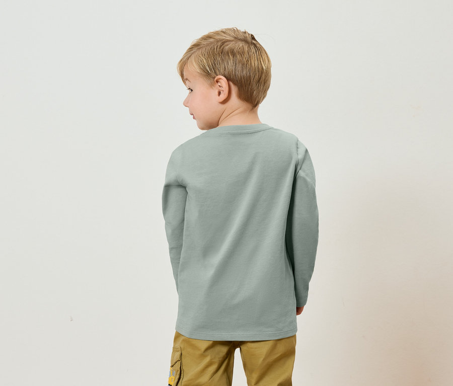 Rückansicht eines Kindes mit blonden Haaren, das ein graues Langarmshirt und Khaki-Hosen trägt.