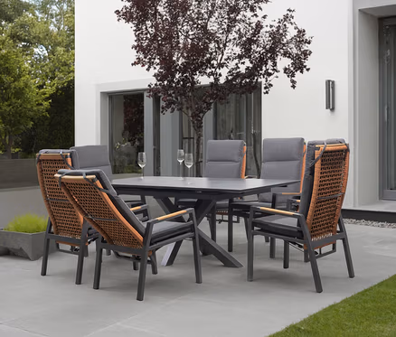 Gartenset mit Esstisch und sechs Stühlen mit grauen Polstern und Rattangeflecht auf einer Terrasse.