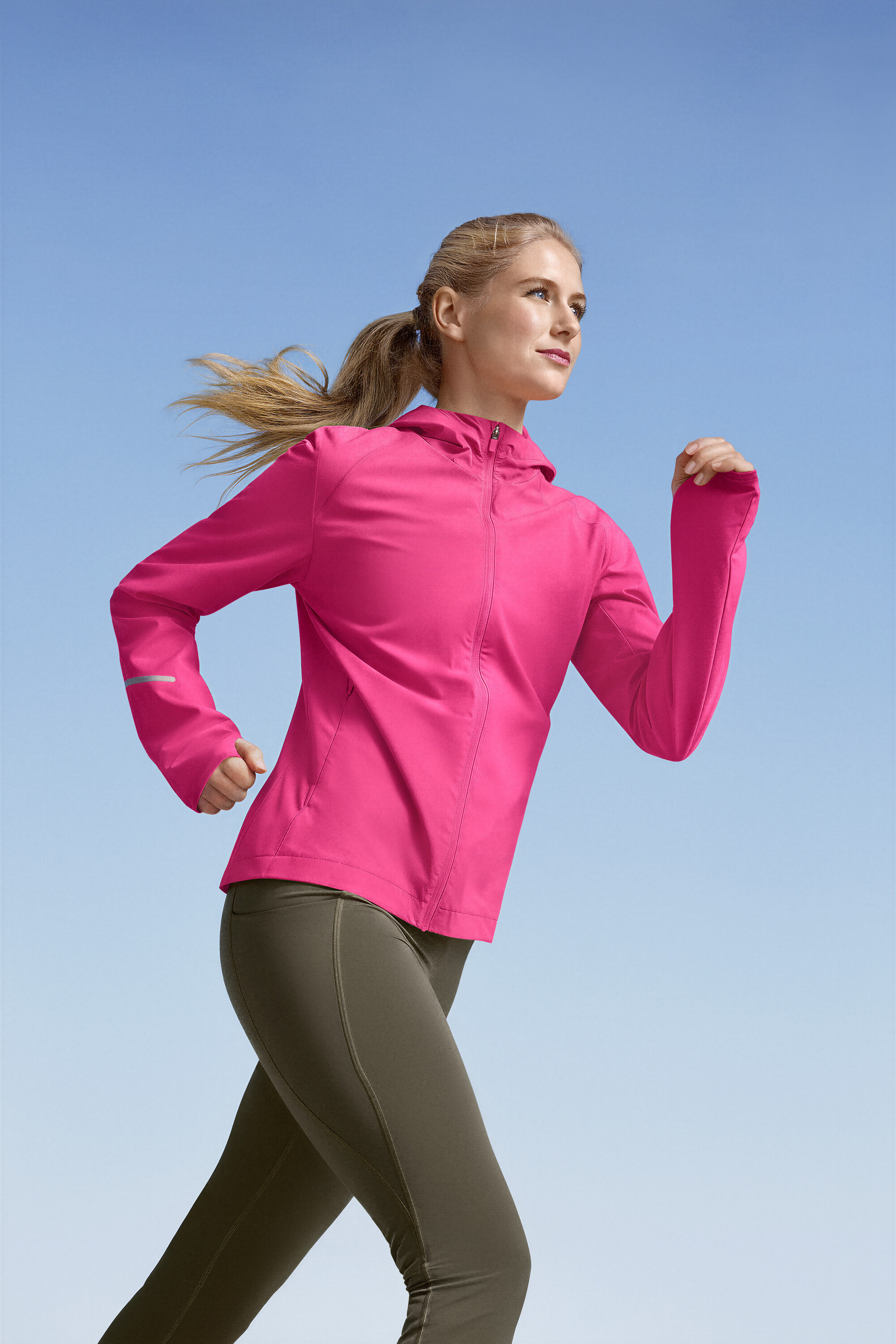 Frau joggt in pinker Laufjacke und grünen Sportleggings »ActivePower« vor blauem Himmel.