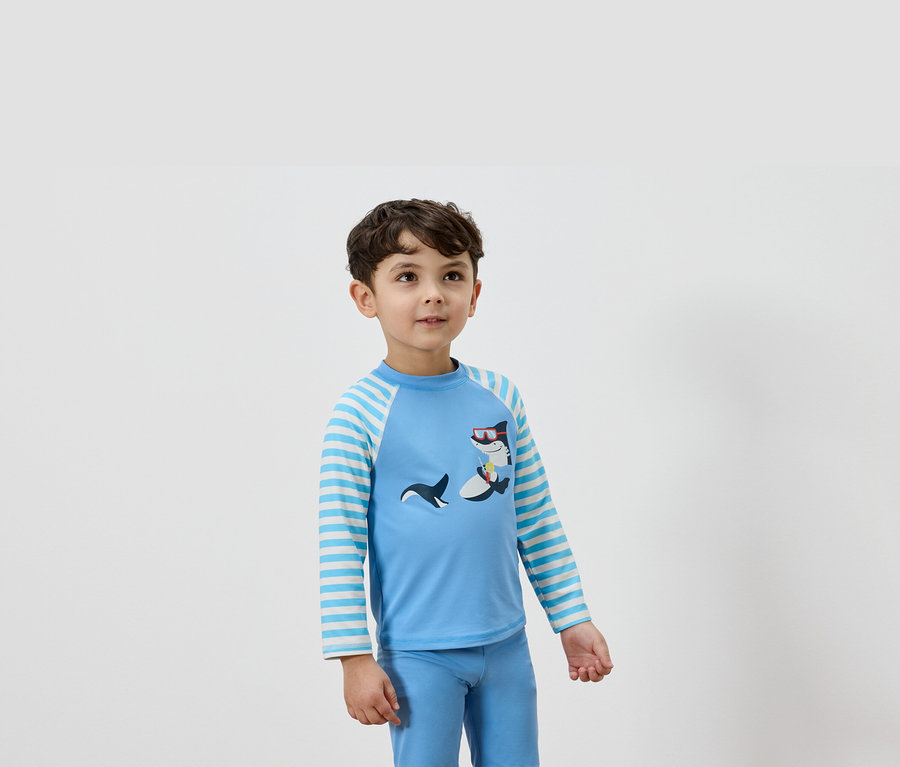 Ein Junge trägt ein hellblaues Langarmshirt mit einem Hai-Design und dazu passende blaue Hosen.