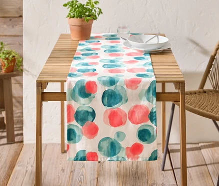 Ein Holztisch mit einer Tischdecke mit blauen und roten Kreisen, Geschirr und einer Topfpflanze darauf.