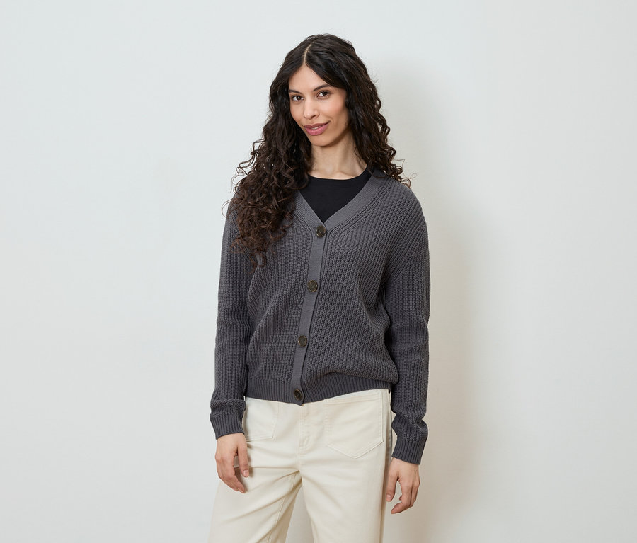 Frau trägt graue Strickjacke mit Knöpfen und helle Hose.
