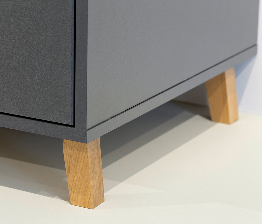 Detailaufnahme eines grauen Schranks mit hellbraunen Holzfüßen auf hellem Untergrund.