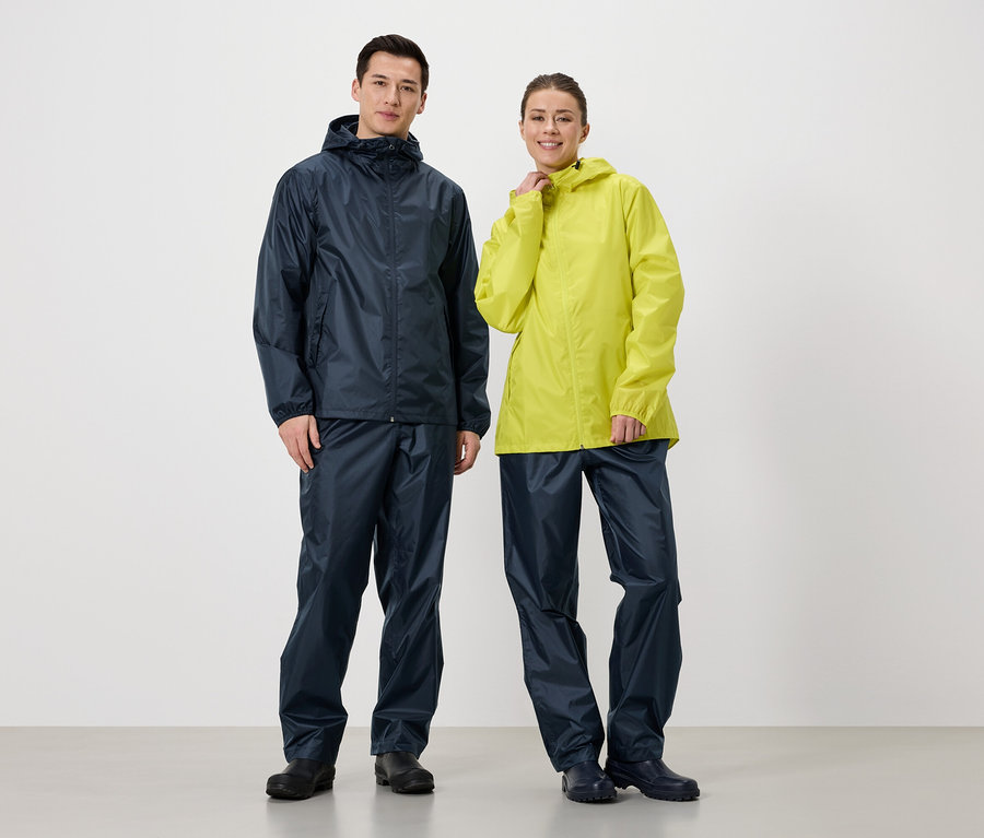Ein Mann in marineblauer Regenjacke und Regenhose steht neben einer Frau in gelber Regenjacke und marineblauer Regenhose.
