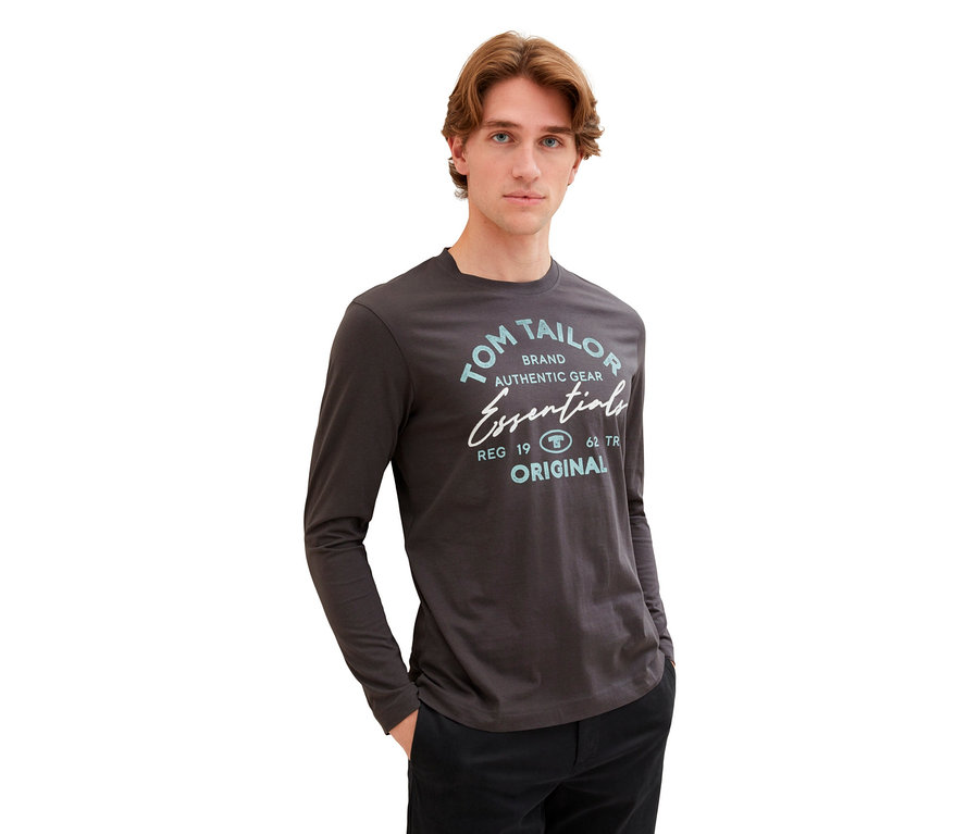 Mann mit Tom Tailor Longsleeve mit Logo, Dark Shadow, mit Händen in den Hosentaschen.