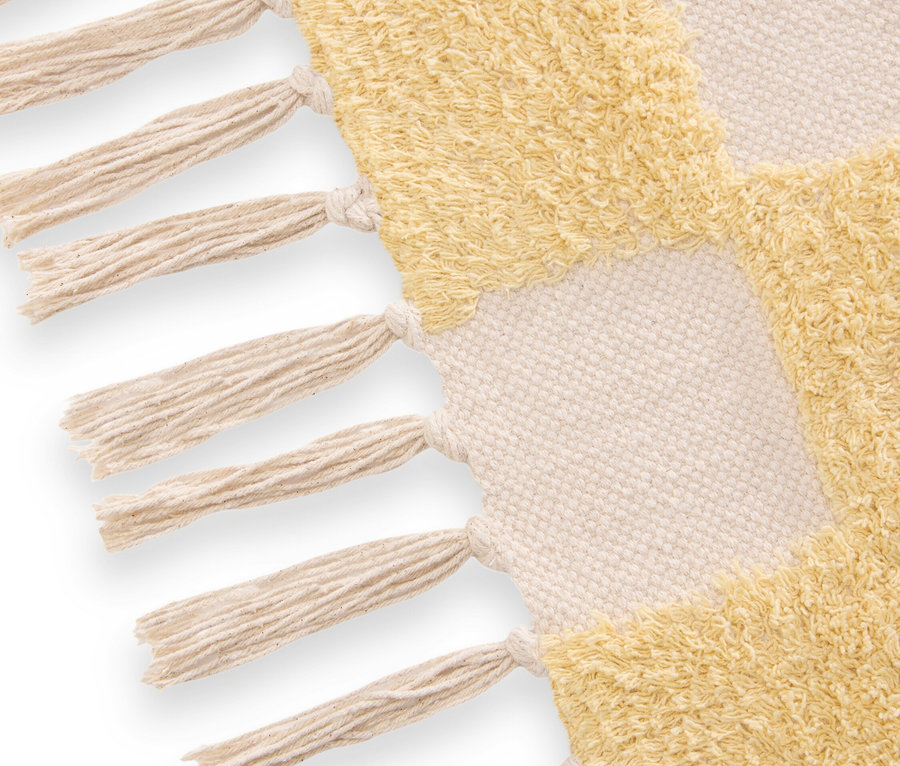 Detailaufnahme eines Teppichs mit gelbem und cremefarbenem Schachmuster und Fransen.