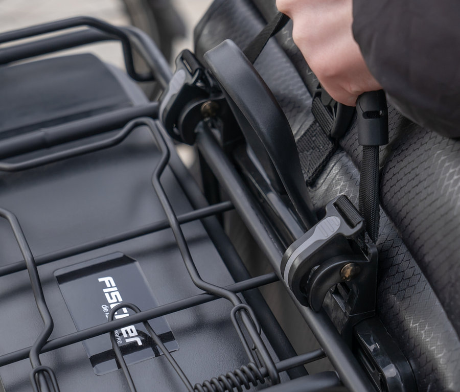 Hand befestigt FISCHER Gepäckträgertasche PLUS+ Terra an einem Fahrradträger.