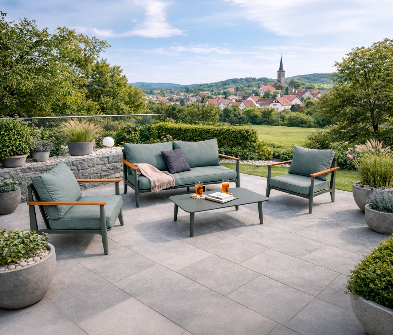Auf einer Terrasse steht ein Leco Lounge-Set inkl. Tisch mit Getränken und einem Buch, im Hintergrund eine Ortschaft.