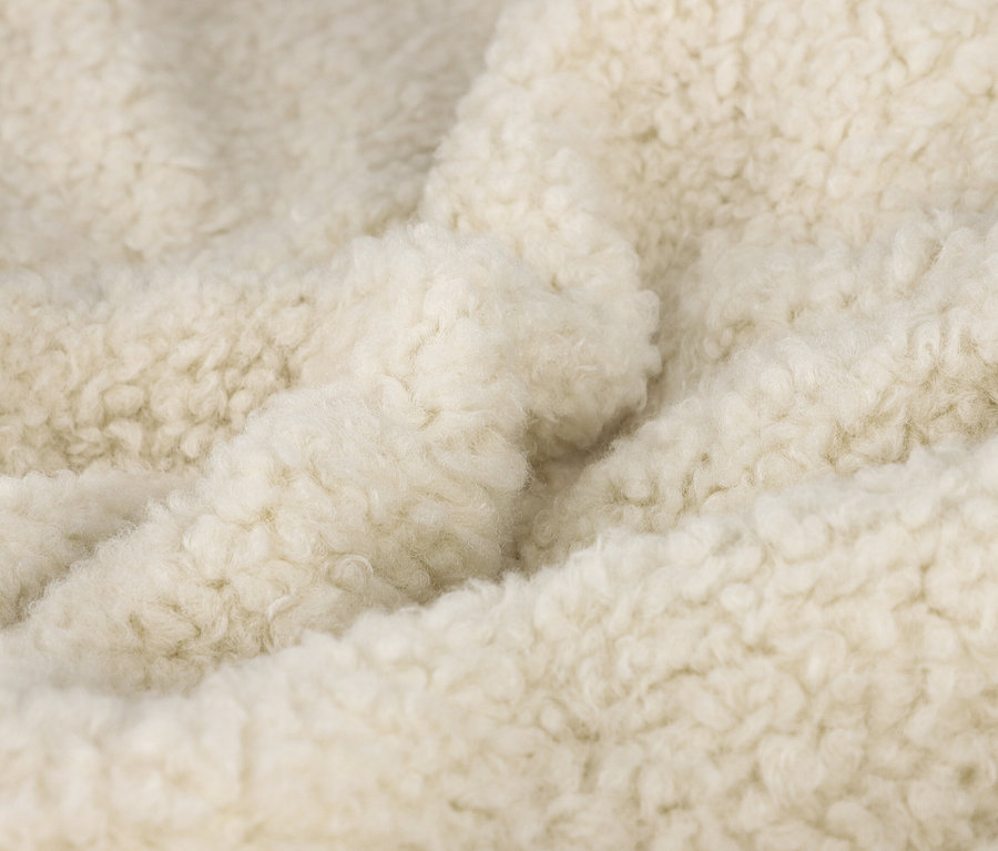 Nahaufnahme eines cremefarbenen, flauschigen Stoffes mit lockiger Textur, der weiche Falten und Knicke zeigt.