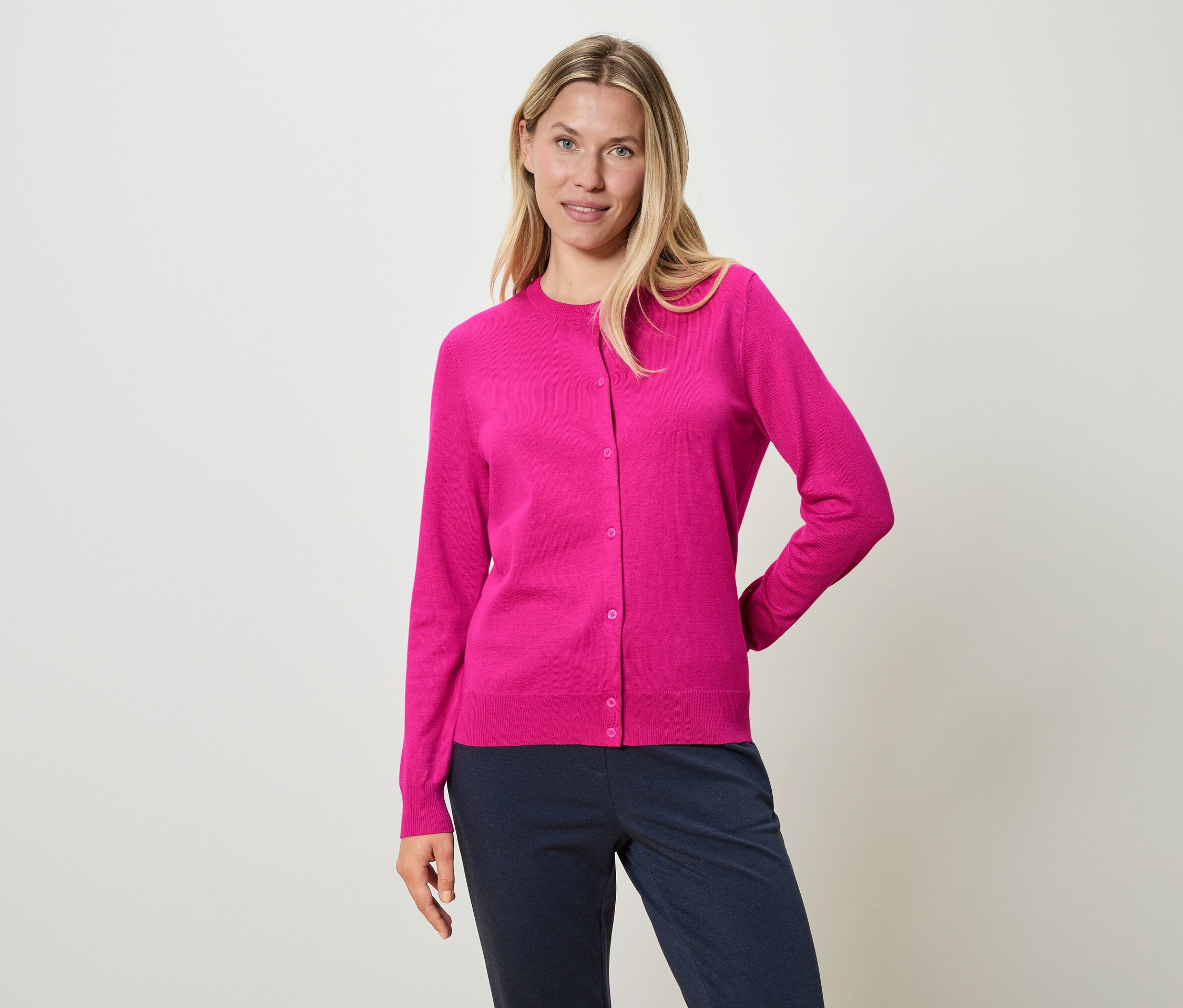 Frau trägt eine pinkfarbene Strickjacke und blaue Hosen.