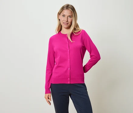 Frau trägt eine pinkfarbene Strickjacke und blaue Hosen.