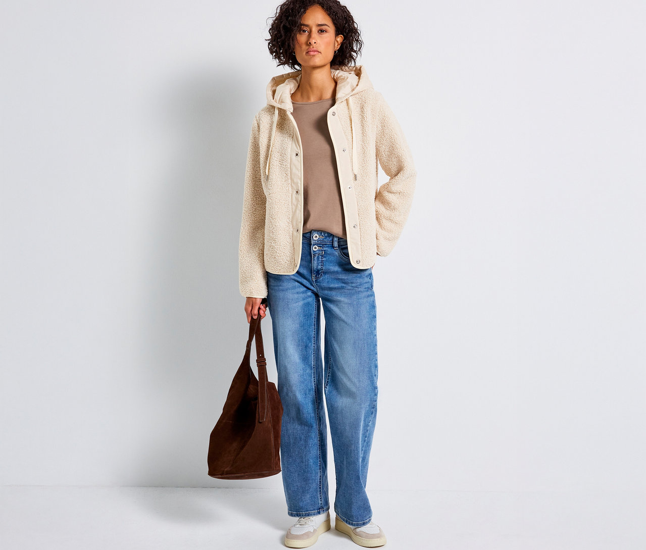 Frau trägt eine Street One Teddyjacke mit abnehmbarer Kapuze, Jeans und hält eine braune Tasche.