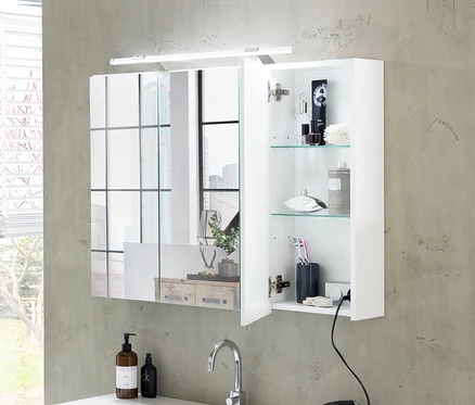 Weißer Spiegelschrank »Dorina« mit Lichtleiste darüber, eine Tür offen, die Toilettenartikel auf Glasböden über einem Waschbecken mit Wasserhahn zeigt.