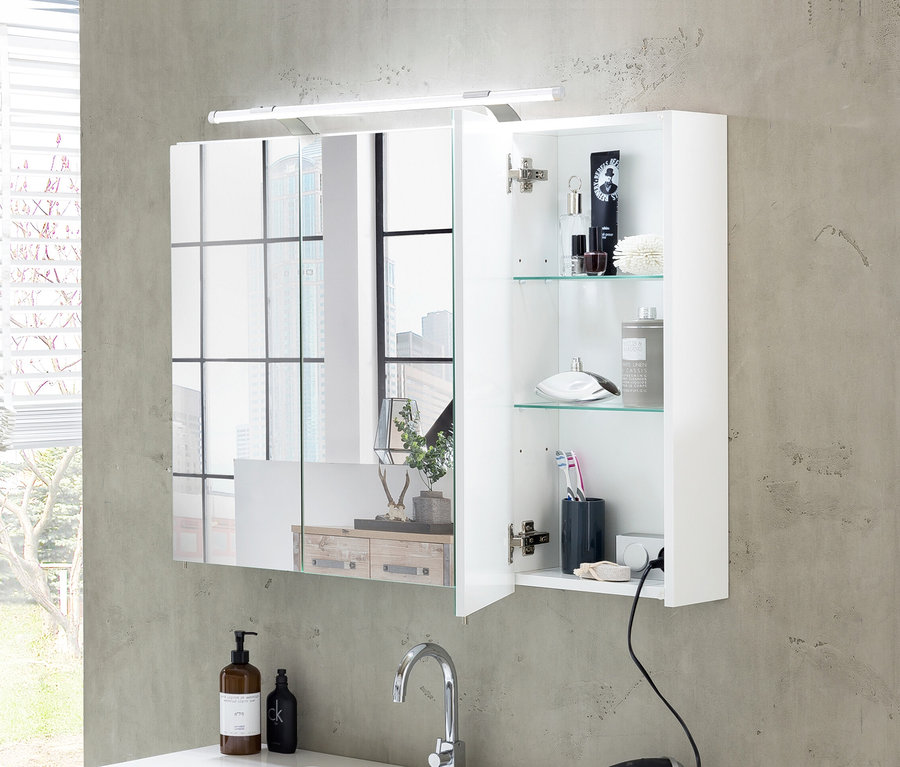 Weißer Spiegelschrank »Dorina« mit Lichtleiste darüber, eine Tür offen, die Toilettenartikel auf Glasböden über einem Waschbecken mit Wasserhahn zeigt.