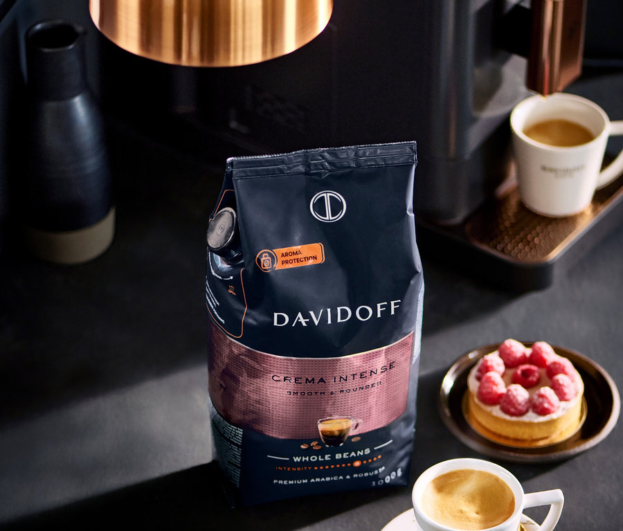 Eine Packung DAVIDOFF CAFÉ Crema Intense 1000 g ganze Bohne steht neben einer Tasse Kaffee und einem Himbeerkuchen.