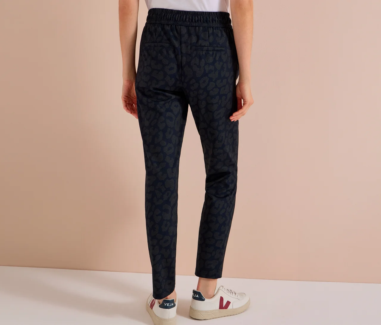 Person von hinten in dunkelblauer CECIL Jerseyhose mit Alloverprint und weißen Sneakern.