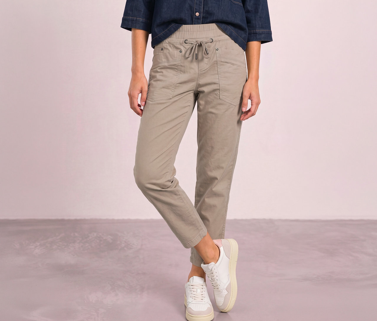 Person trägt beigefarbene Street One Bonny Hose mit Kordelzug, ein Jeanshemd und weiße Sneaker.