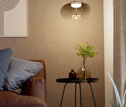 Ein gemütliches Wohnzimmer mit braunem Ledersofa, einem schwarzen Beistelltisch mit zwei Vasen und einer modernen Pendelleuchte aus Rauchglas. An der Wand hängt ein abstraktes Bild.