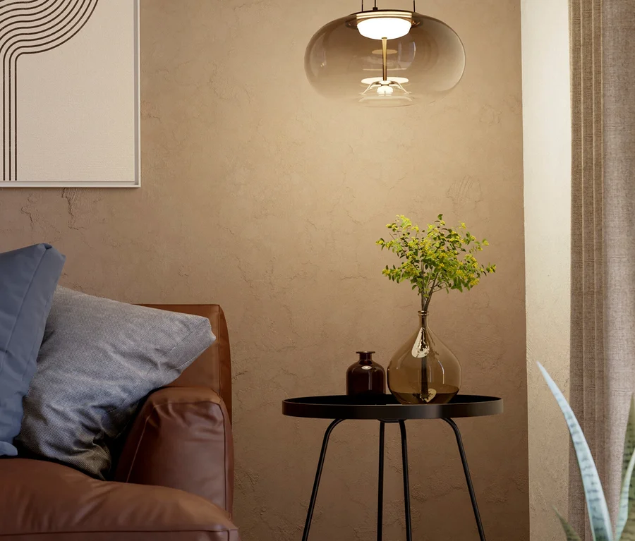 Ein gemütliches Wohnzimmer mit braunem Ledersofa, einem schwarzen Beistelltisch mit zwei Vasen und einer modernen Pendelleuchte aus Rauchglas. An der Wand hängt ein abstraktes Bild.