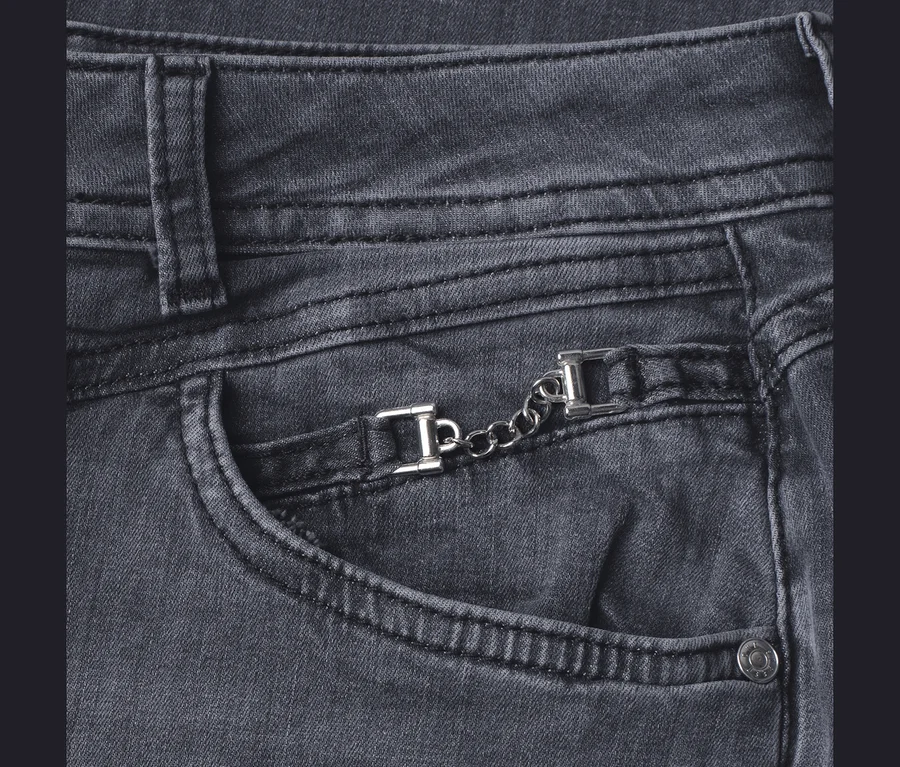 Nahaufnahme einer grauen Street One Jeans, die eine Vordertasche mit einer dekorativen silberfarbenen Kette und zwei rechteckigen Schnallen darüber zeigt.