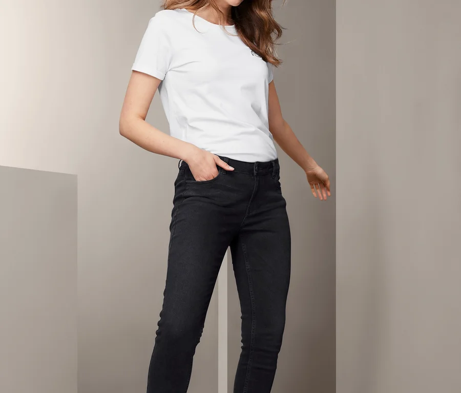 Frau posiert in schwarzen Skinny-Jeans und weißem T-Shirt.