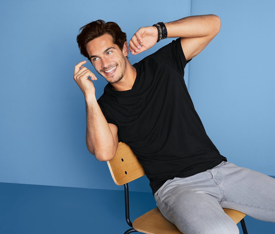 Mann sitzt auf Stuhl und trägt schwarzes 2 T-Shirts mit V-Ausschnitt.