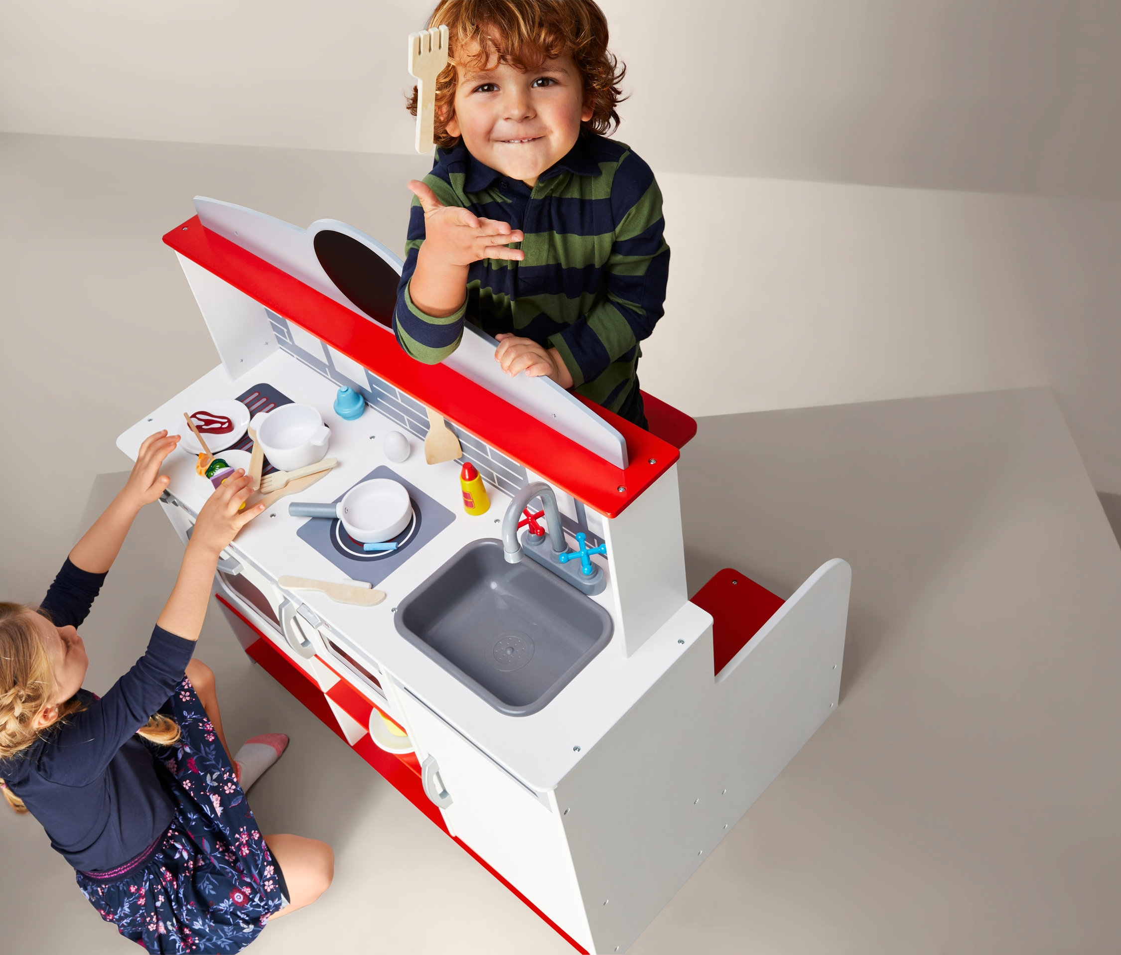 Kinder spielen mit der 2-in-1-Restaurant-Spielküche. Ein Junge hält eine Holzzgabel, während ein Mädchen mit Essen auf der Küchenzeile spielt.