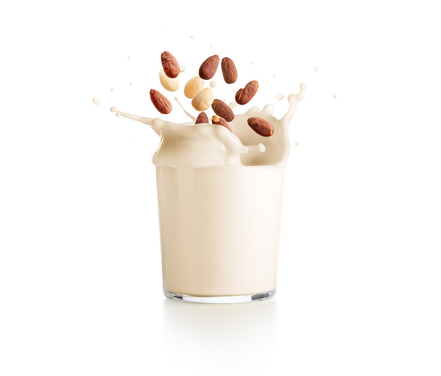 Mandeln fallen in ein Glas Pflanzenmilch.