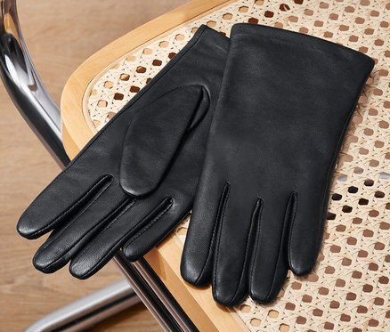 Schwarze Lederhandschuhe liegen auf einem Rattanstuhl.