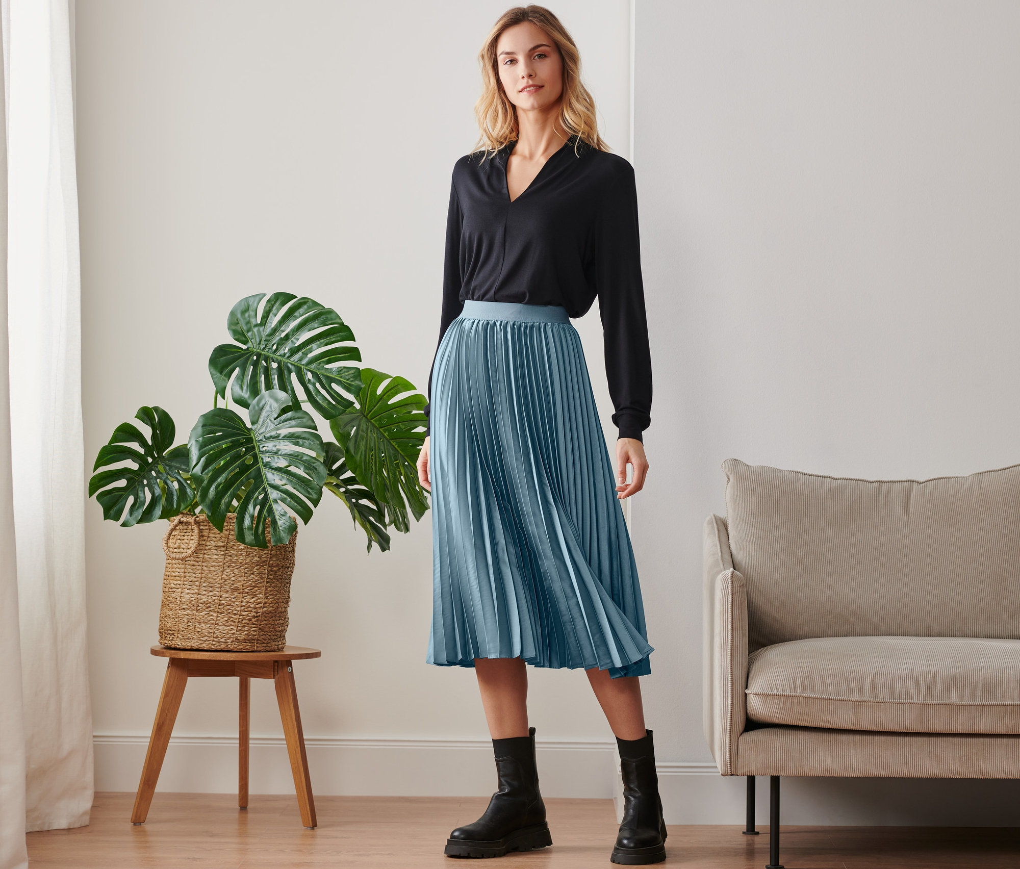 Frau posiert in schwarzem Oberteil und Plisseerock.