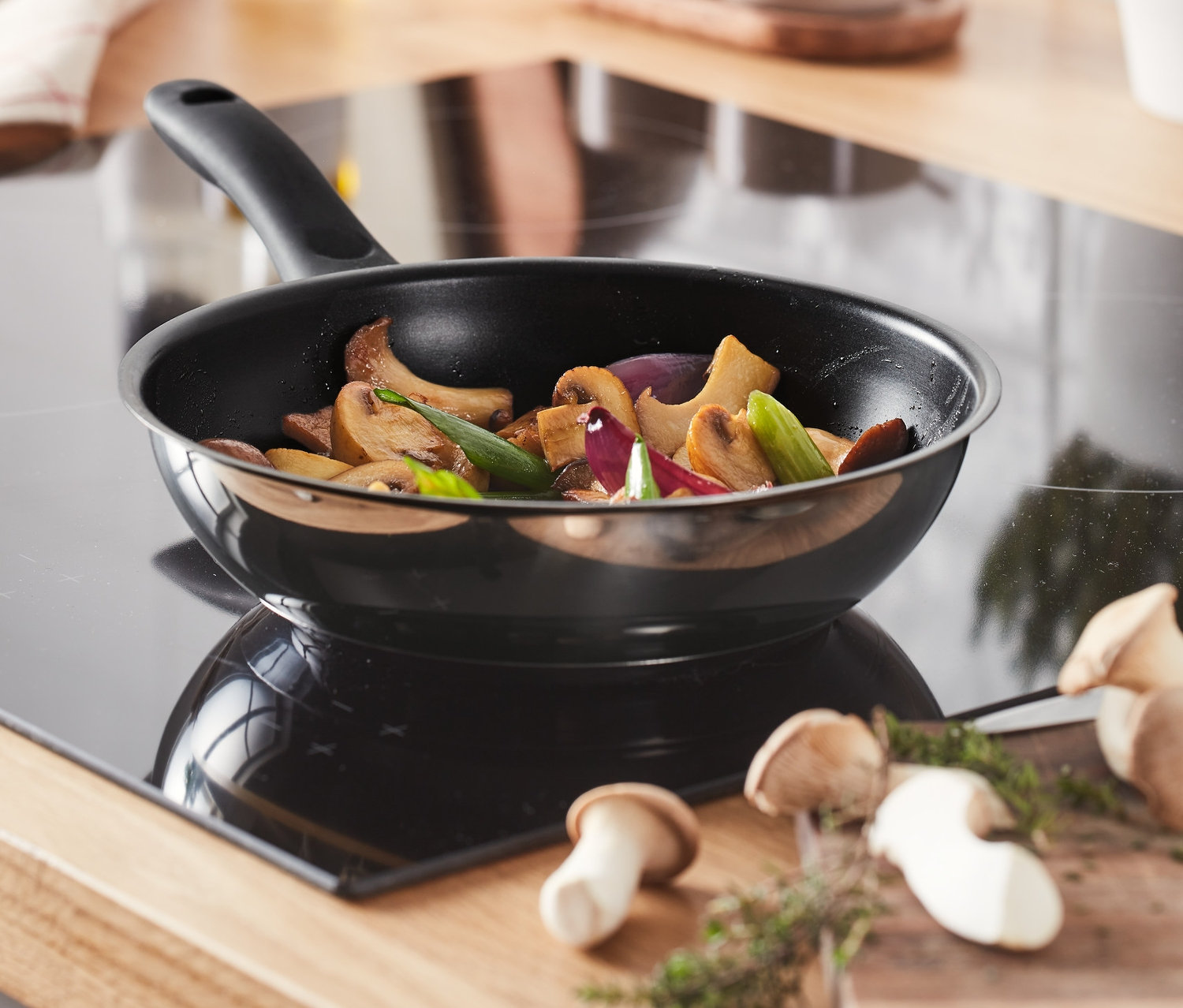 Auf einem Kochfeld steht eine ca. 20 cm große Edelstahl-Pfanne, in der Gemüse angebraten wird.