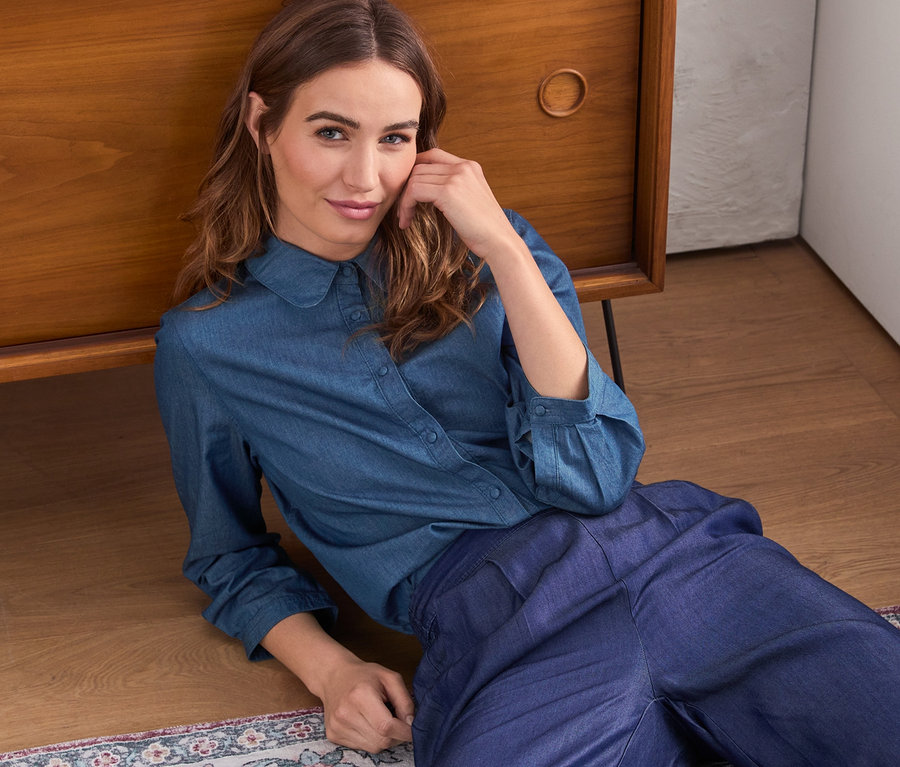 Frau liegt am Boden und trägt eine Jeans-Hemdbluse.
