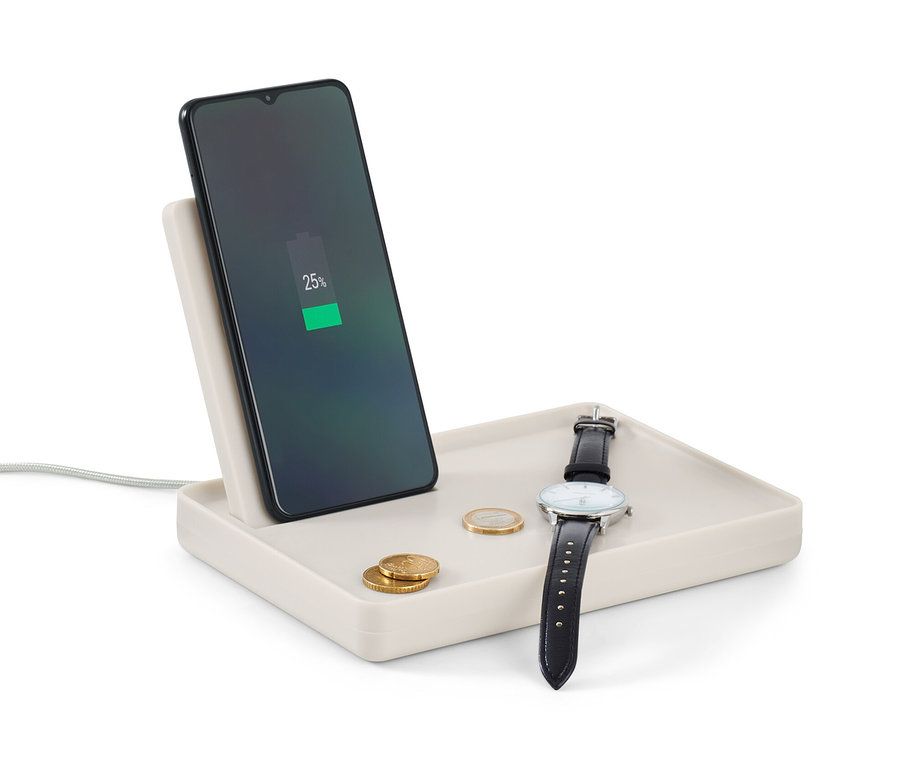 Handy lädt auf Ablage mit kabelloser Ladefunktion. Auf der Ablage liegen eine Uhr und Münzen.
