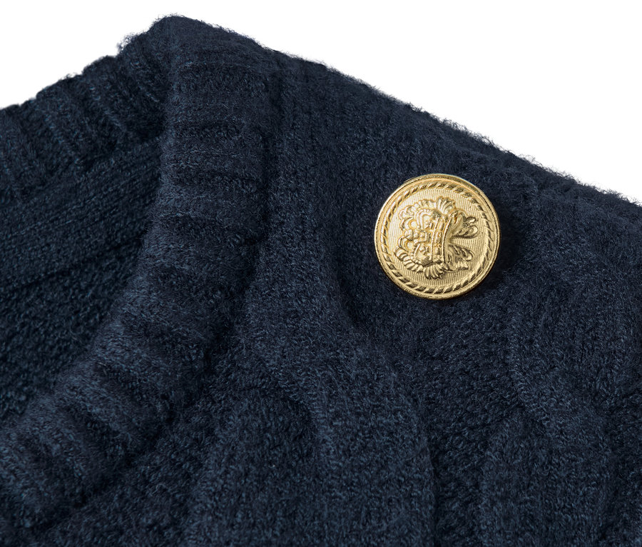 Detailansicht eines Zopfpullovers mit einem dekorativen goldenen Knopf.