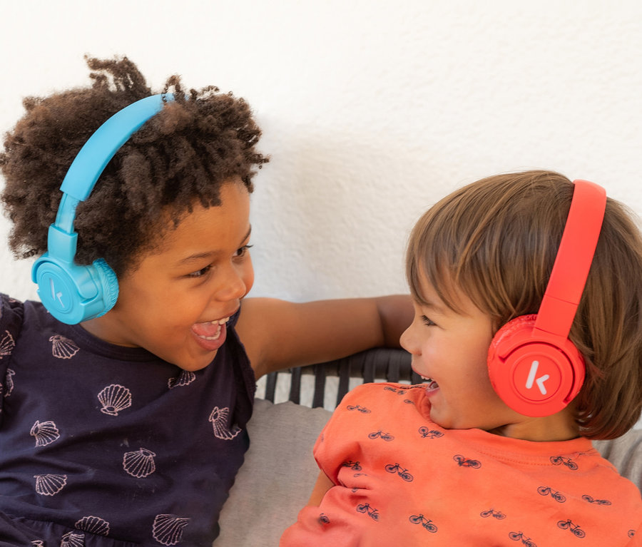 Zwei Kinder lachen sich an und tragen Kekz-Kopfhörer. Ein Kind trägt blaue, das andere rote Kopfhörer.