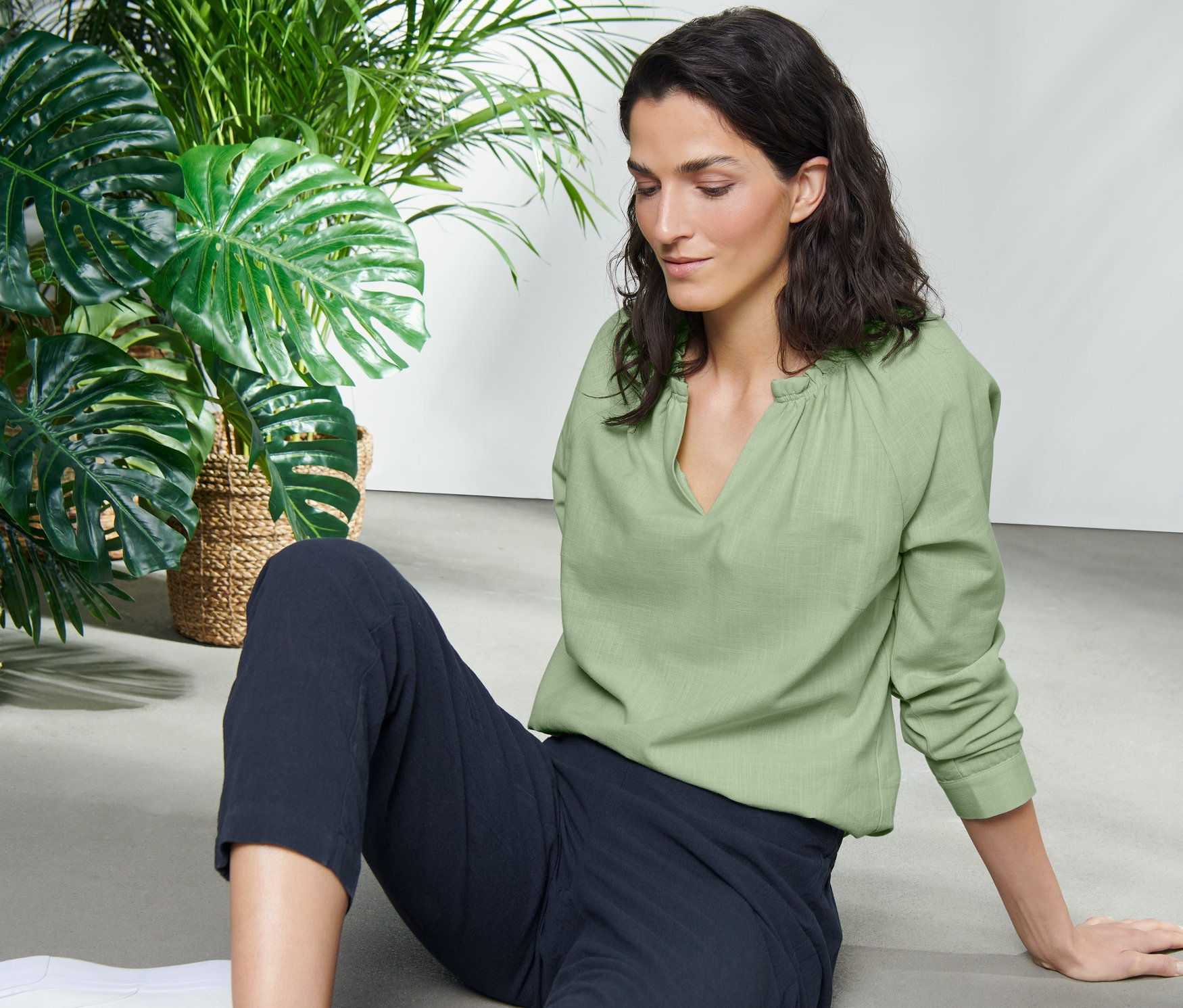 Frau sitzt auf dem Boden und trägt eine hellgrüne Bluse mit V-Ausschnitt.