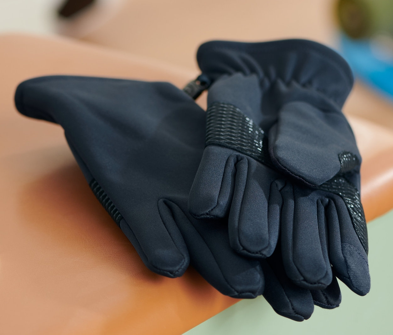 Zwei Softshell-Handschuhe liegen auf einem kleinen Hocker. Im Hintergrund sind ein Fußball und ein Skateboard zu sehen.