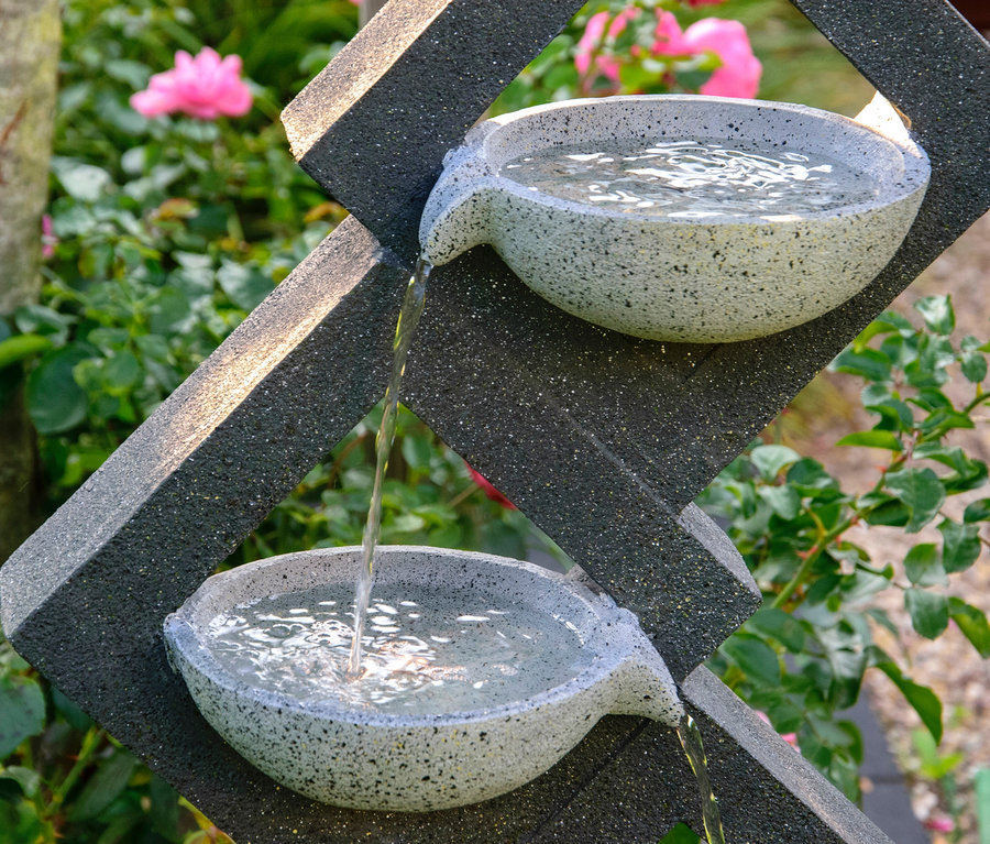 Wasser fließt aus zwei Steinschalen des Dobar Gartenbrunnens mit 4 Schalen und LEDs.