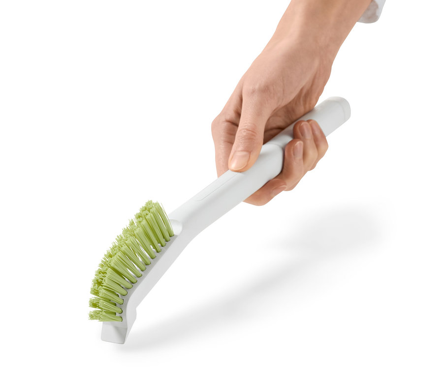 Eine Hand hält eine lange Fugenbürste mit weißem Griff und grünen Borsten.