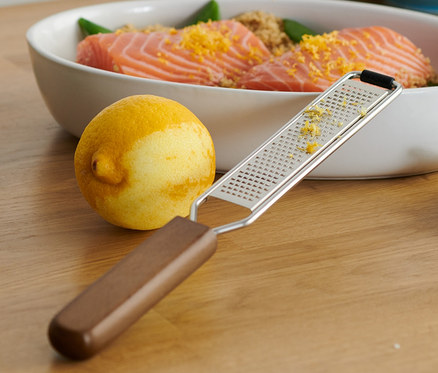 Auf einem Holztisch liegt eine Schüssel mit Lachs und daneben eine Handreibe, fein.
