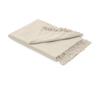 Eine beige Chenille-Wohndecke mit Fransen liegt gefaltet auf einem weißen Hintergrund.