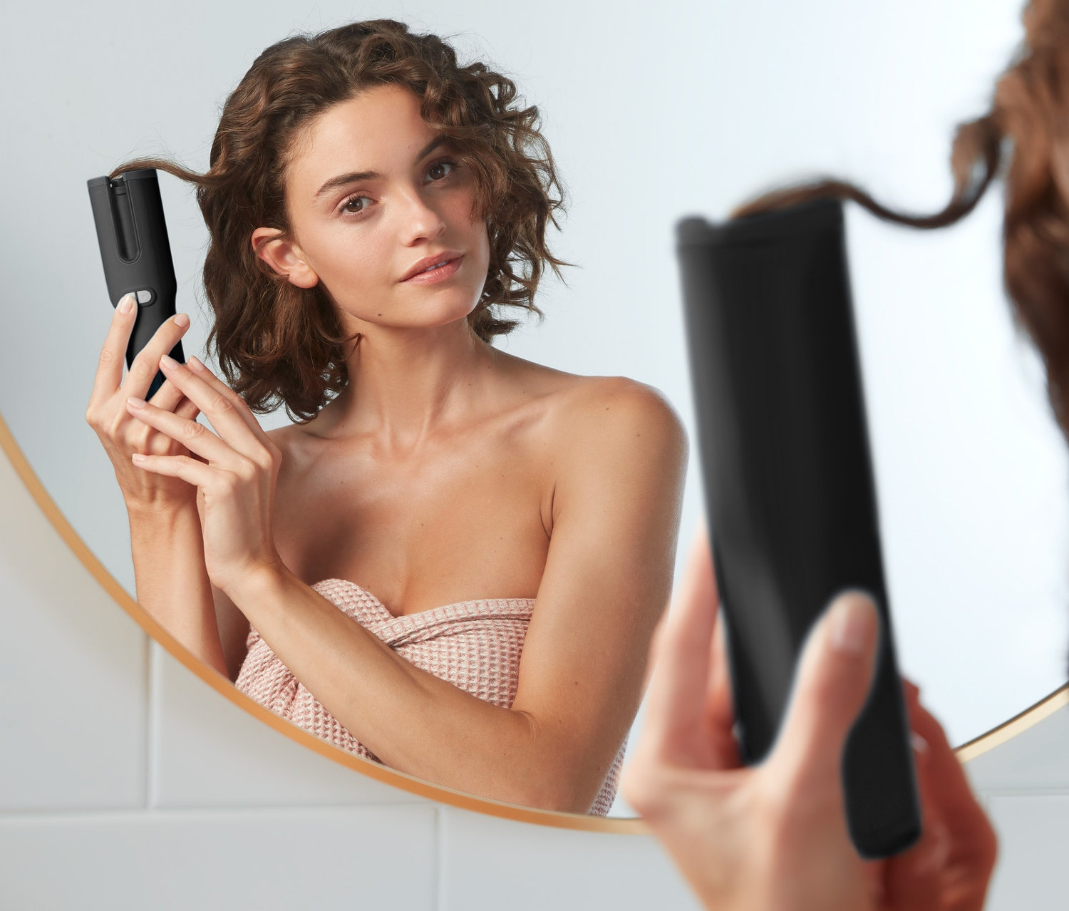 Frau benutzt einen automatischen Lockenstyler vor einem Spiegel.