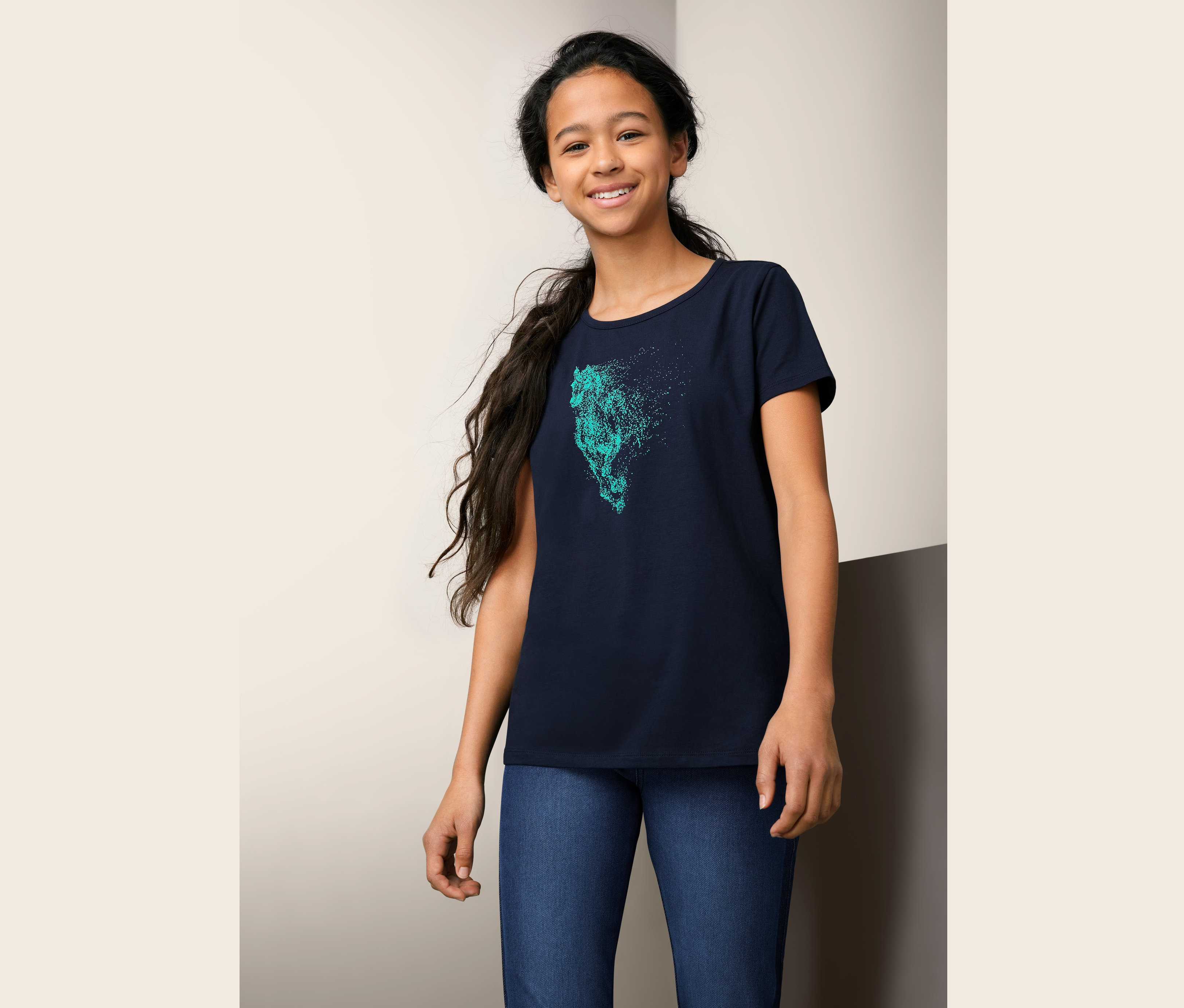 Lächelndes junges Mädchen trägt ein blaues T-Shirt mit Pferdeaufdruck. 2 T-Shirts