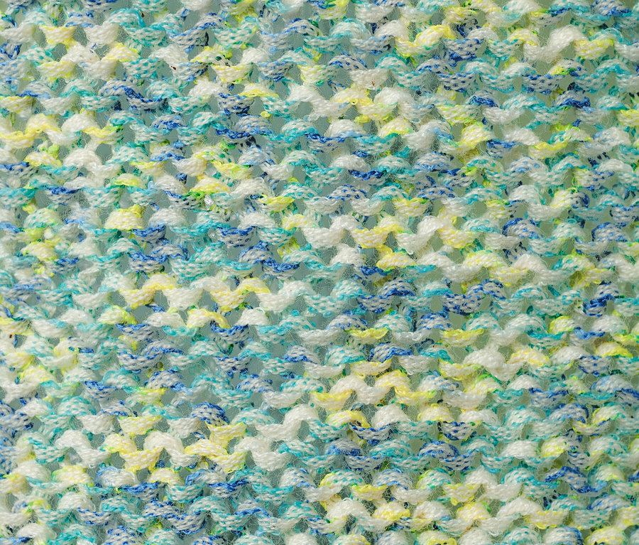 Nahaufnahme eines Strickpullovers aus Bändchengarn mit blauen, gelben und weißen Fäden.