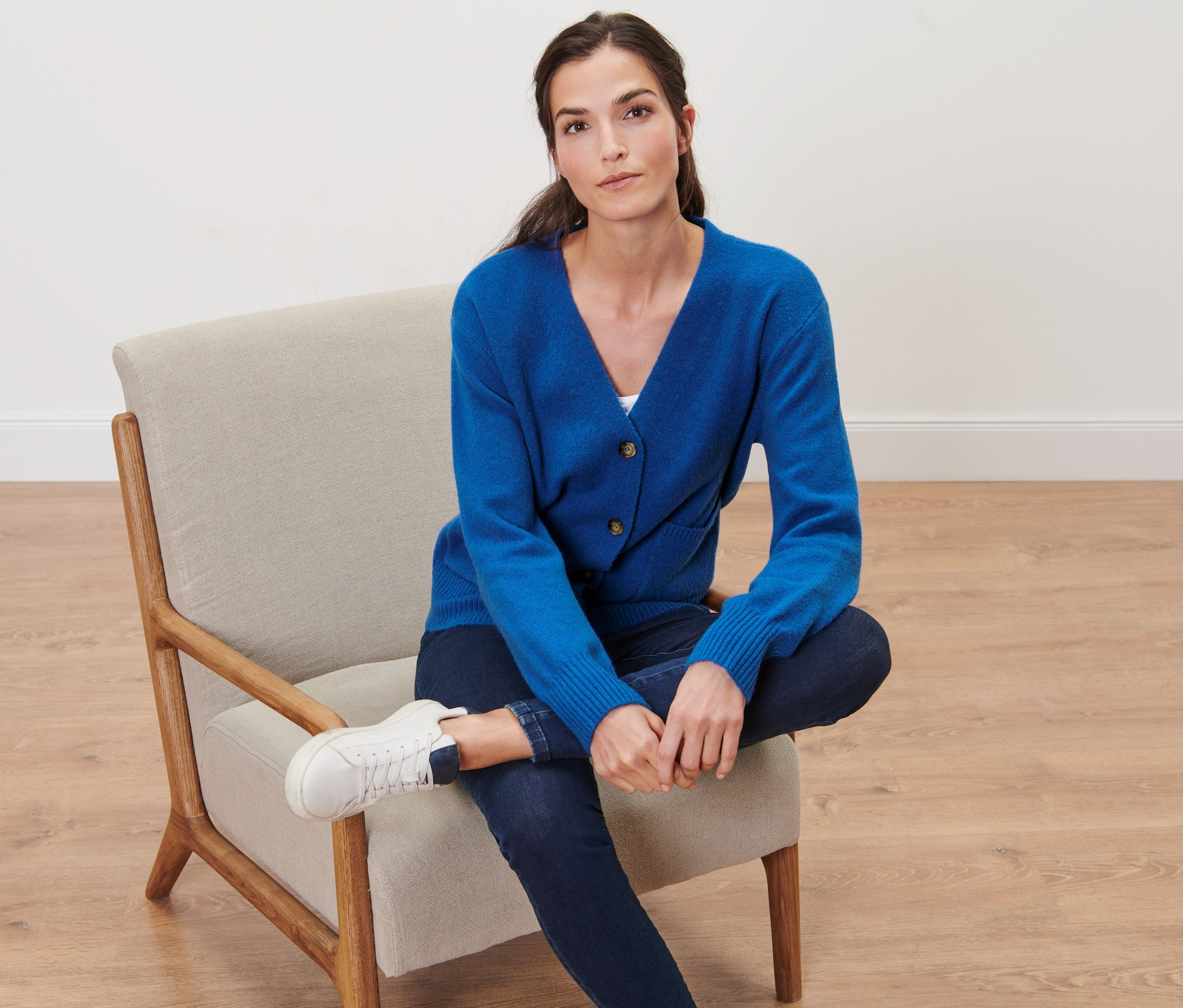 Frau sitzt im Sessel und trägt eine Strickjacke mit Wolle, kobaltblau.