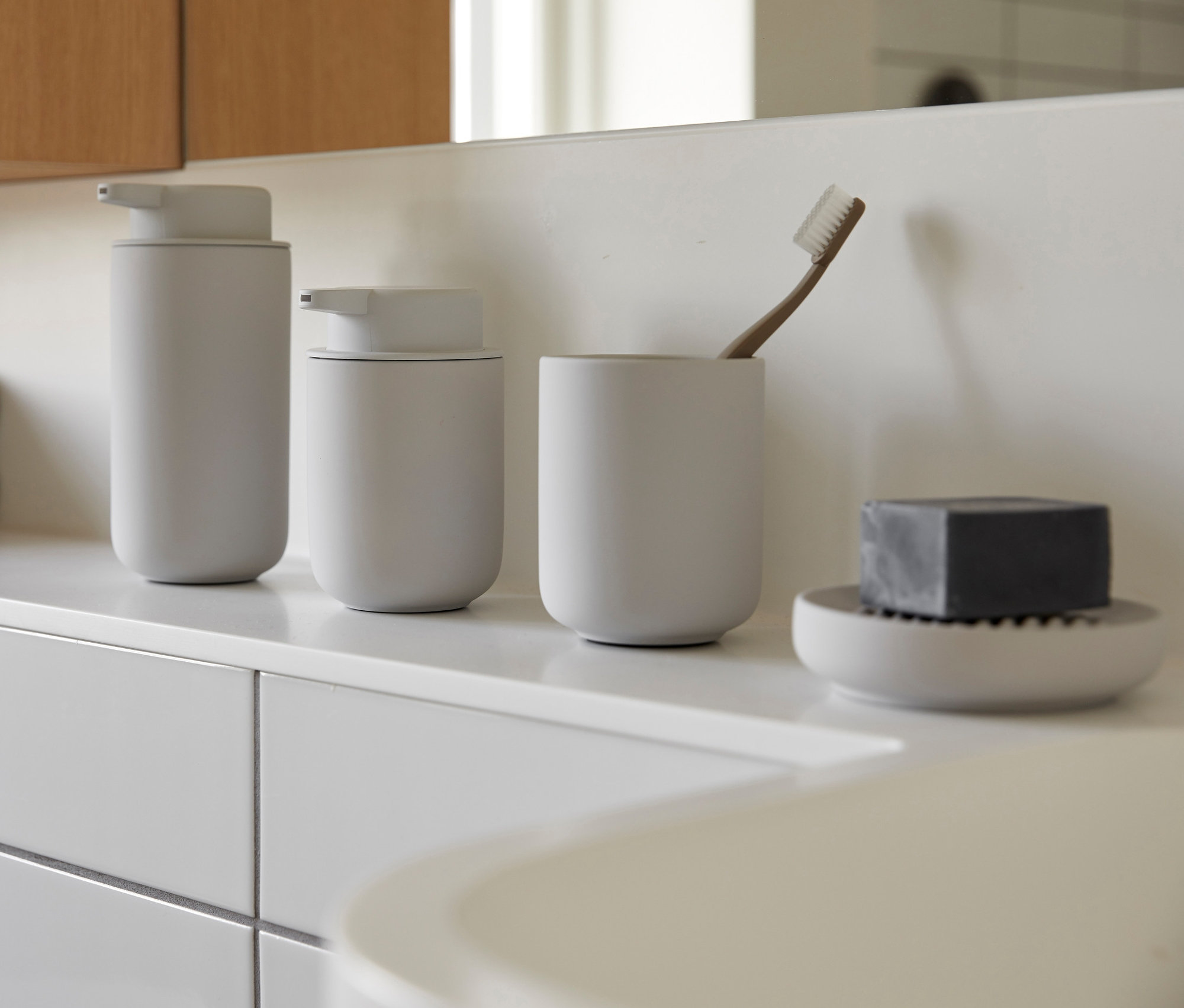 Auf einem weißen Regal stehen ein grauer ZONE DENMARK Seifenspender »Ume«, ein Becher mit einer Zahnbürste und eine Schale mit Seife.