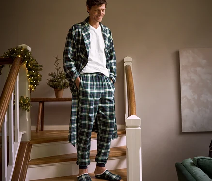 Ein Mann geht eine Treppe hinunter, trägt einen karierten Flanell-Morgenmantel, eine Flanell-Relaxhose, Hausschuhe und 2 T-Shirts mit V-Ausschnitt.