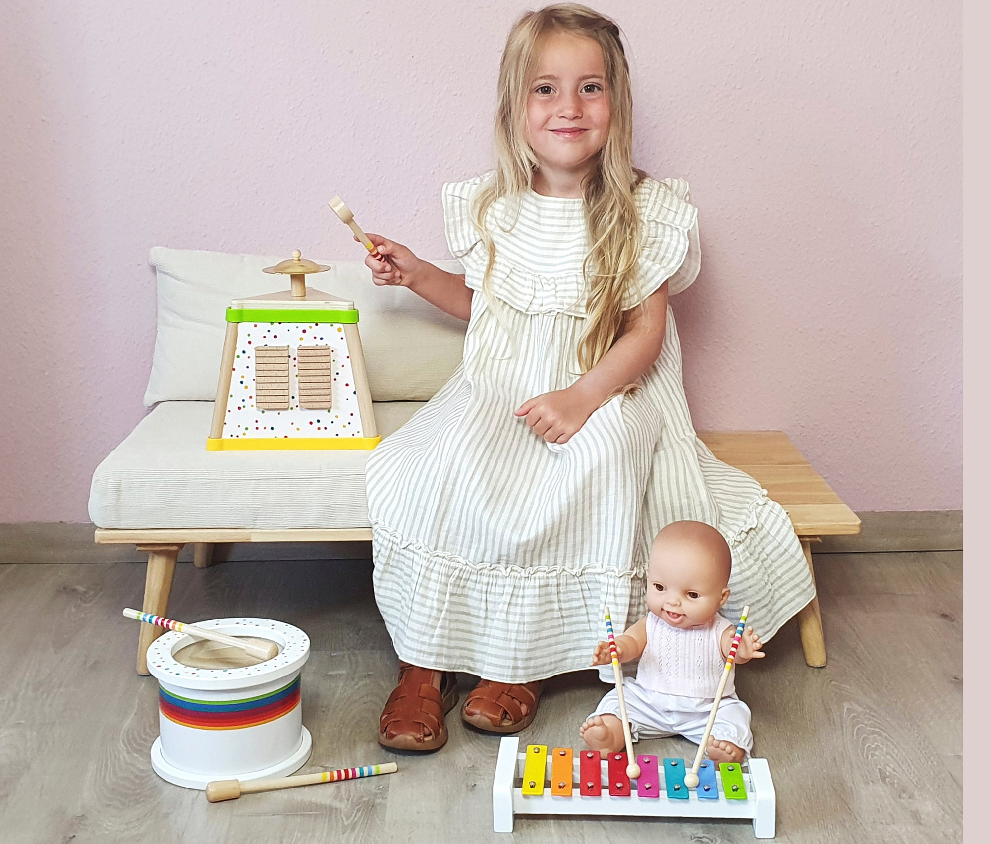 Mädchen sitzt auf Bank mit Musikspielzeugen inklusive small foot Musikdreieck »Sound«.