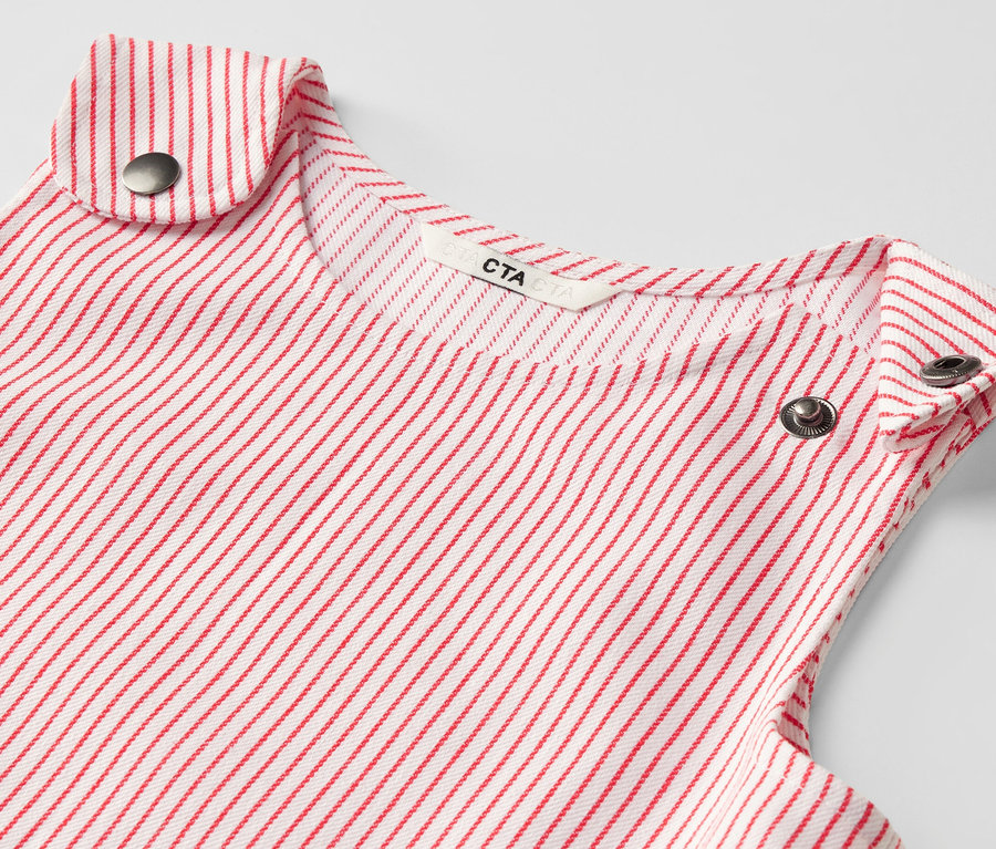 Detailaufnahme eines Kinder-Web-Latzkleids mit roten Streifen und Metallknöpfen.